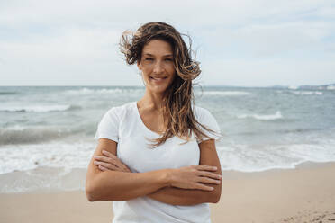 Smiling woman standing with arms crossed at beach - JOSEF16249