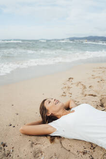 Frau mit Händen hinter dem Kopf auf Sand am Meer liegend am Strand - JOSEF16261