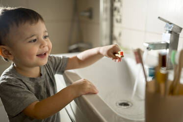 Glücklicher Junge mit Zahnbürste am Waschbecken im Bad - ANAF00950