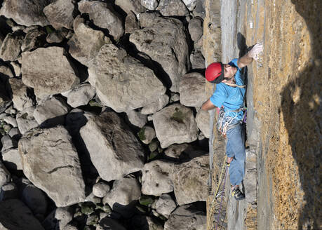 Sportler klettert an einem sonnigen Tag an einer Felswand - ALRF01915