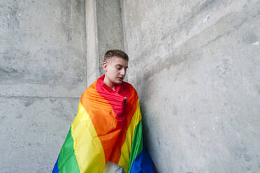 Nicht-binäre Person in Regenbogenflagge an der Wand eingewickelt - ASGF03266