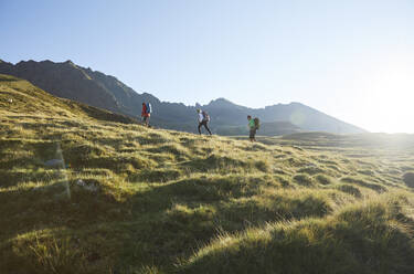 Österreich, Tirol, Sonne beleuchtet Wanderer, die im Sommer durch grüne Alpenlandschaft wandern - CVF02220