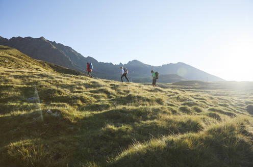 Österreich, Tirol, Sonne beleuchtet Wanderer, die im Sommer durch grüne Alpenlandschaft wandern - CVF02220