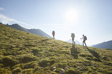 Österreich, Tirol, Sonne beleuchtet Wanderer, die im Sommer durch grüne Alpenlandschaft wandern - CVF02222