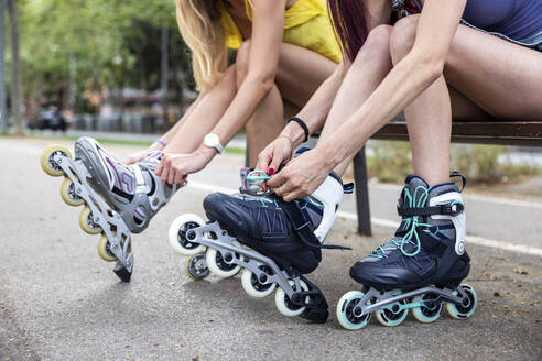 Frauenhände beim Binden der Schnürsenkel von Inline-Skates auf einer Bank sitzend - WPEF07123