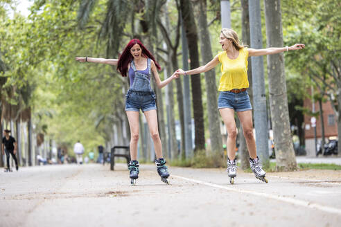 Freunde halten sich an den Händen und genießen es, auf der Straße zu skaten - WPEF07126