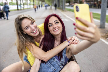 Glückliche Frau mit Freund nimmt Selfie durch Handy auf Bank - WPEF07133