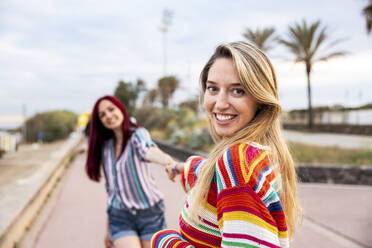 Glückliche Freunde halten sich an der Promenade an der Hand - WPEF07171