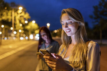 Lächelnde Frau mit Smartphone und Freund im Hintergrund - WPEF07191