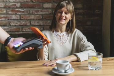 Lächelnde Frau beim Bezahlen mit dem Smartphone in einem Café - OSF01360