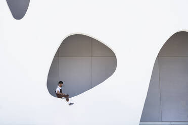 Young man with laptop sitting on wall - JCZF01143