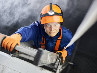 Industrial worker wearing hard hat and climbing harness ascending ladder - CVF02225