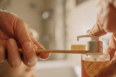 Hands of man putting toothpaste on brush in bathroom - ANAF00954