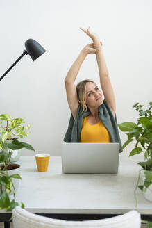 Contemplative woman stretching arms at desk in home office - SVKF01164