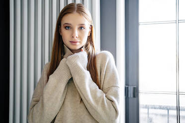 Selbstbewusstes Teenager-Mädchen mit Pullover vor einem Fenster zu Hause - MDOF00538