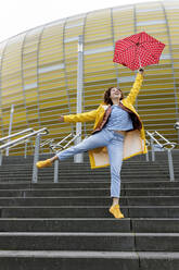 Carefree woman holding umbrella jumping on steps - VIVF00328