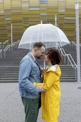 Lächelndes Paar unter Regenschirm auf dem Fußweg am Stadion - VIVF00329
