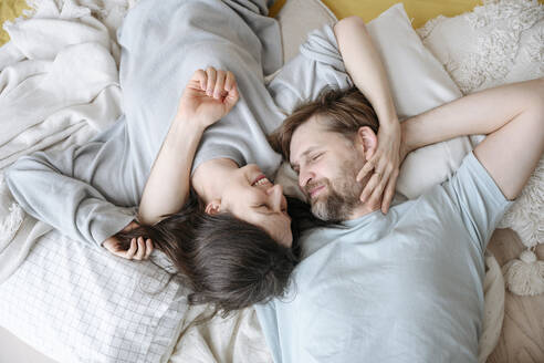 Smiling couple lying together on cushions at home - EYAF02541