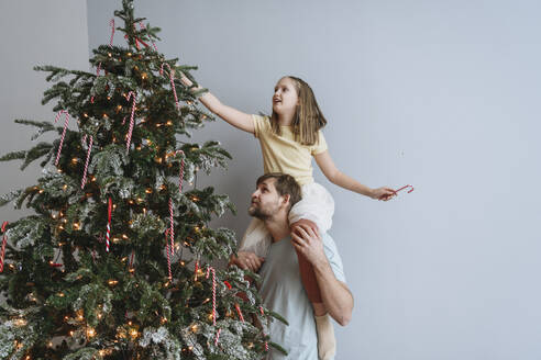 Father carrying daughter on shoulders for decorating Christmas tree at home - EYAF02551