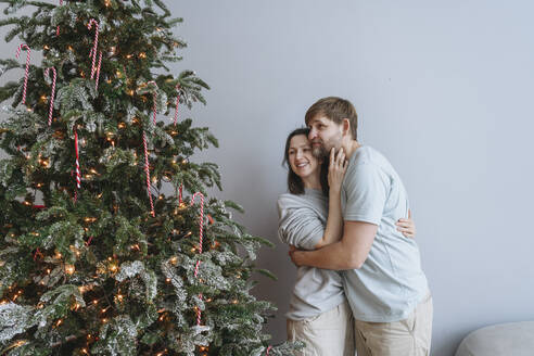 Couple embracing and looking at Christmas tree - EYAF02553