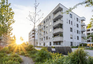 Deutschland, Bayern, München, Wohngarten vor modernem Mehrfamilienhaus bei Sonnenuntergang - MAMF02545