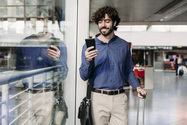 Happy businessman using smart phone at railroad station - EBBF07756