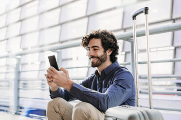 Glücklicher Geschäftsmann mit Smartphone am Bahnhof - EBBF07762