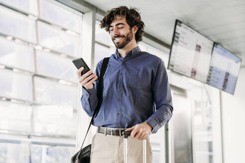 Smiling young businessman using mobile phone at station - EBBF07767