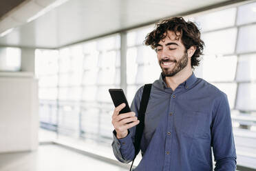 Glücklicher junger Geschäftsmann, der ein Mobiltelefon am Bahnhof benutzt - EBBF07771