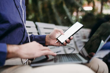 Young businessman with smart phone using laptop - EBBF07793