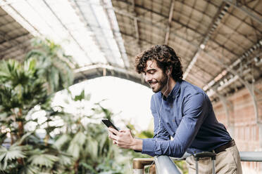 Smiling businessman wearing in-ear headphones using smart phone at station - EBBF07805