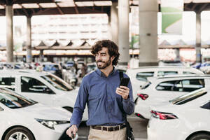 Happy businessman standing in front of cars on road - EBBF07818