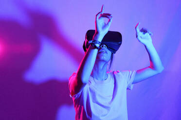 Young woman with VR Goggles gesturing over neon colored background - JSMF02629