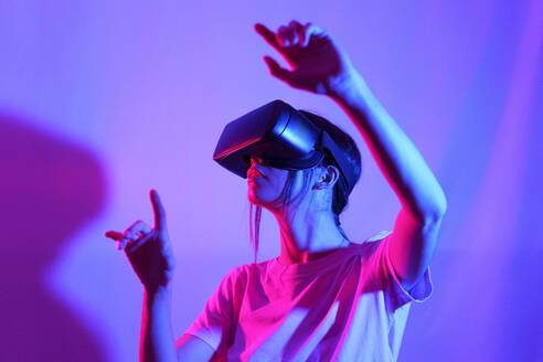 Frau beobachtet VR-Brille und gestikuliert vor farbigem Hintergrund - JSMF02630