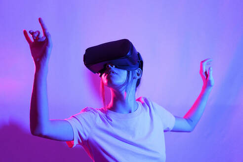 Junge Frau, die mit einer VR-Brille beobachtet und über einen neonfarbenen Hintergrund gestikuliert - JSMF02631