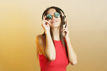 Smiling woman wearing steampunk sunglasses and listening music on headphones - JSMF02640