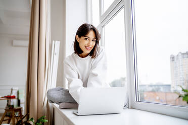Happy beautiful woman sitting with laptop at home - MDOF00552