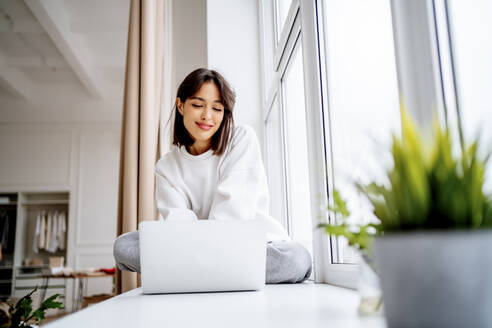 Smiling young woman using laptop at home - MDOF00553