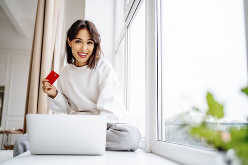 smiling young woman shopping with credit card on laptop at home - MDOF00560
