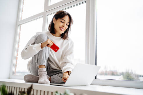 Glückliche schöne Frau beim Online-Shopping mit Kreditkarte über Laptop - MDOF00562