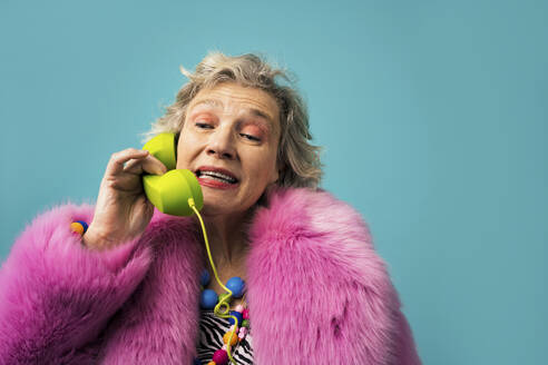Frau mit Pelzmantel spricht am Telefon vor farbigem Hintergrund - OIPF02978