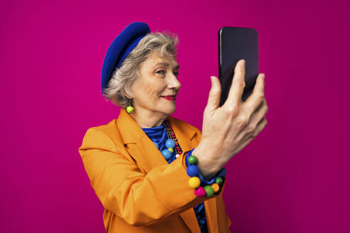 Senior Influencer macht Selfie mit Smartphone vor rosa Hintergrund - OIPF02994