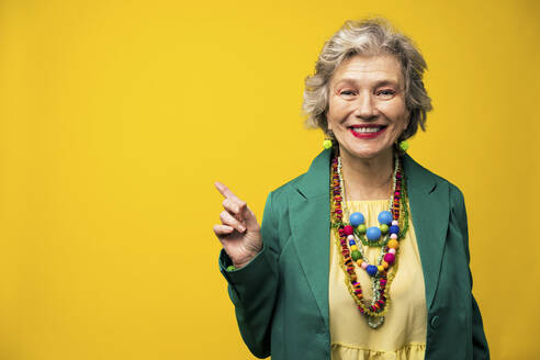 Lächelnde ältere Frau, die auf einen gelben Hintergrund zeigt - OIPF03007