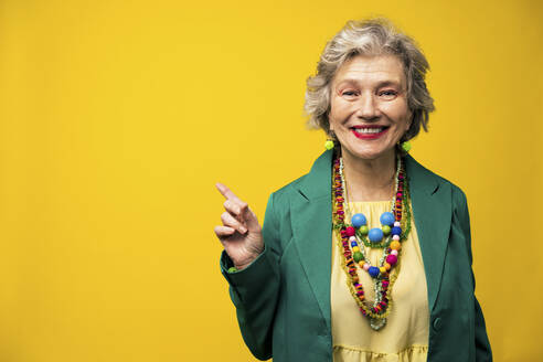 Smiling senior woman pointing against yellow background - OIPF03007