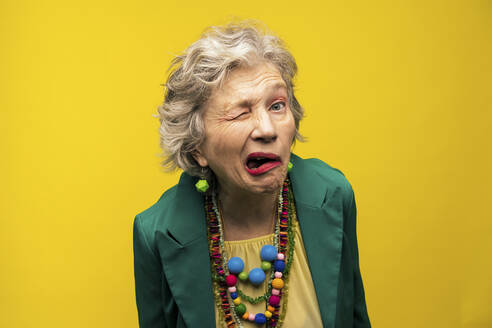 Senior woman making funny faces against yellow background - OIPF03012