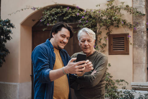 Glücklicher Mann mit Vater, der vor dem Haus ein Smartphone benutzt - JOSEF16272