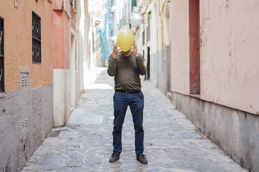 Mann bedeckt Gesicht mit gelbem Luftballon auf der Straße - JOSEF16277