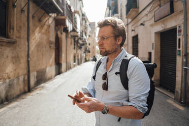 Thoughtful mature man standing with smart phone on street - JOSEF16285