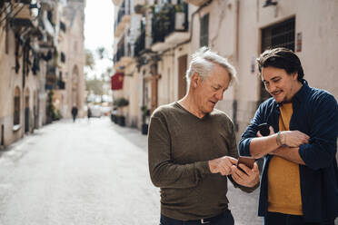 Lächelnder Mann, der mit seinem Vater über ein Smartphone auf der Straße diskutiert - JOSEF16308