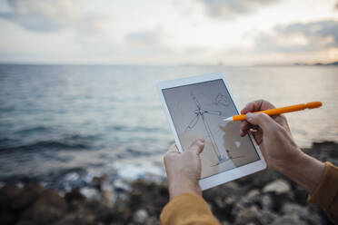 Hände eines älteren Mannes, der mit einem digitalisierten Stift eine Windkraftanlage auf einem Tablet-PC zeichnet - JOSEF16309